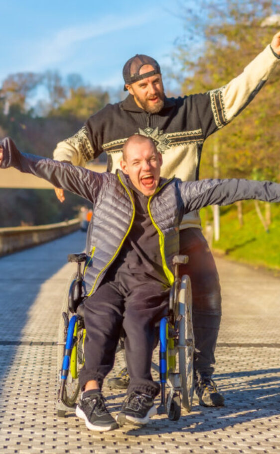 Disabled person in wheelchair with friend overjoyed, smiling, enjoying with arms up, vistoria, enjoying life in sunset of the city
